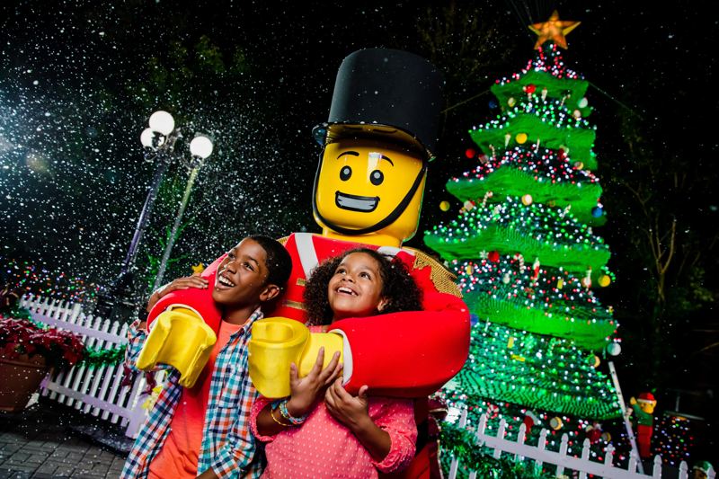A family hugging a LEGO toy soldier next to a LEGO Christmas tree